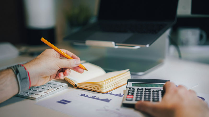 Homme écrivant dans son carnet le résultat de sa calculatrice.