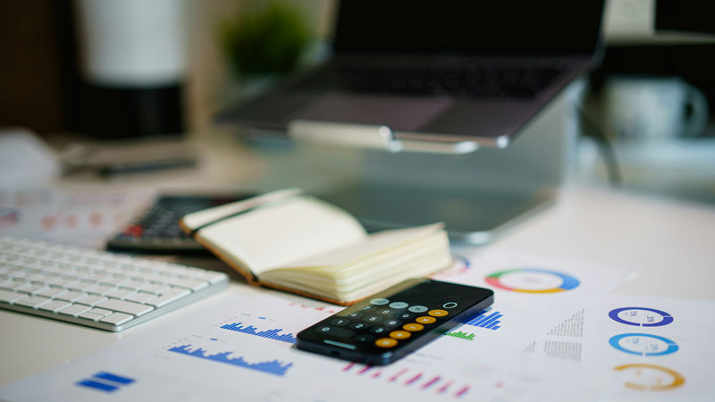 Feuilles de données comptables sur une table avec une calculatrice, un carnet ouvert et un laptop - Exact Online analytique